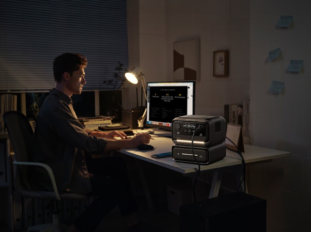 Male guy working in front of desktop using Compact RIVER 3 MAX battery generator with integrated carry handle powering a handheld radio and LED lantern during a nighttime search-and-rescue operation.”